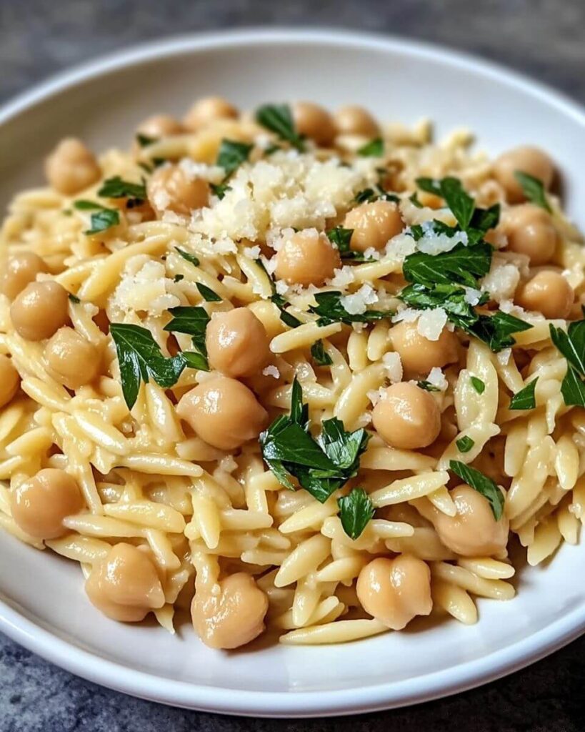 A creamy lemon ricotta orzo dish in a wide bowl, garnished with fresh basil, parsley, and lemon wedges.