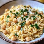 Creamy Lemon Ricotta Orzo with Chickpeas dish in a wide bowl, garnished with fresh basil, parsley, and lemon wedges.