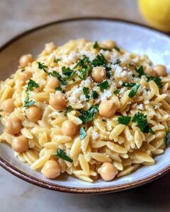 Creamy Lemon Ricotta Orzo with Chickpeas dish in a wide bowl, garnished with fresh basil, parsley, and lemon wedges.