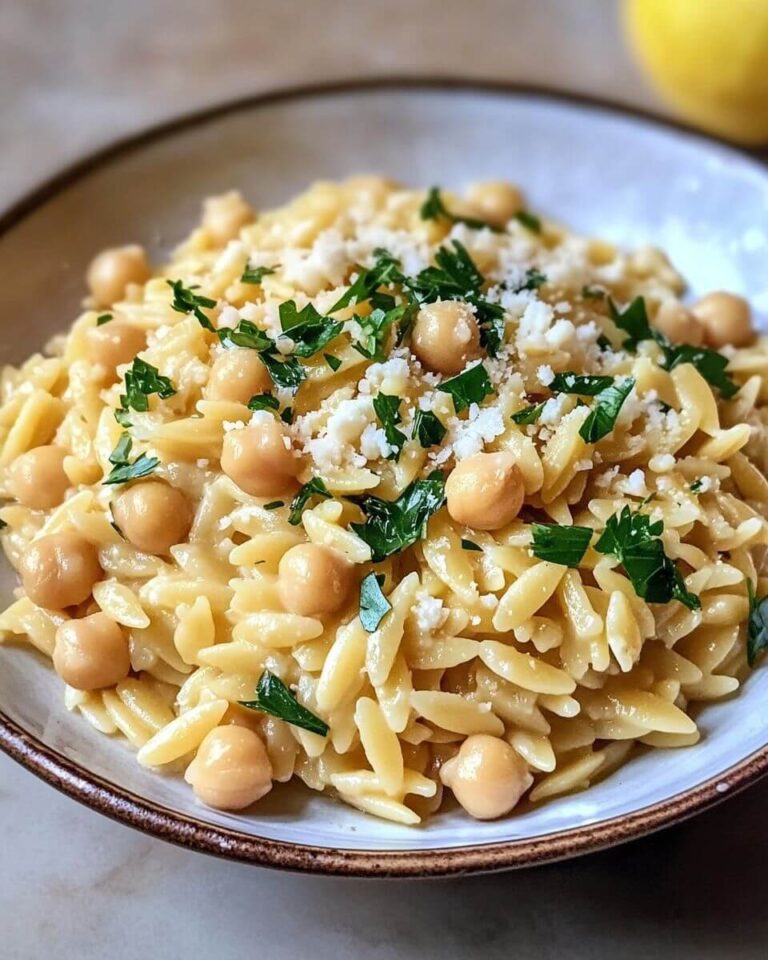Creamy Lemon Ricotta Orzo with Chickpeas dish in a wide bowl, garnished with fresh basil, parsley, and lemon wedges.