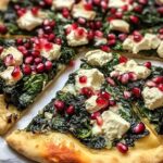 A golden, rustic pizza topped with vibrant winter greens, glistening pomegranate seeds, melted cheese, and red onion slices, fresh out of the oven.
