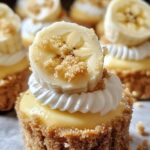 Mini banana pudding cheesecakes topped with whipped cream, fresh banana slices, and vanilla wafers on a white serving platter.