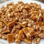 Golden praline crunch clusters with pecans on a white plate, glistening with caramel coating.