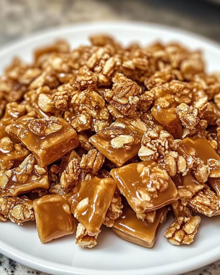 Golden praline crunch clusters with pecans on a white plate, glistening with caramel coating.