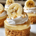 Mini banana pudding cheesecakes topped with whipped cream, fresh banana slices, and vanilla wafers on a white serving platter.